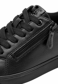 Sneaker in pelle nera con lacci spessi, zip laterale e dettagli lucidi del marchio sulla linguetta, su uno sfondo bianco.