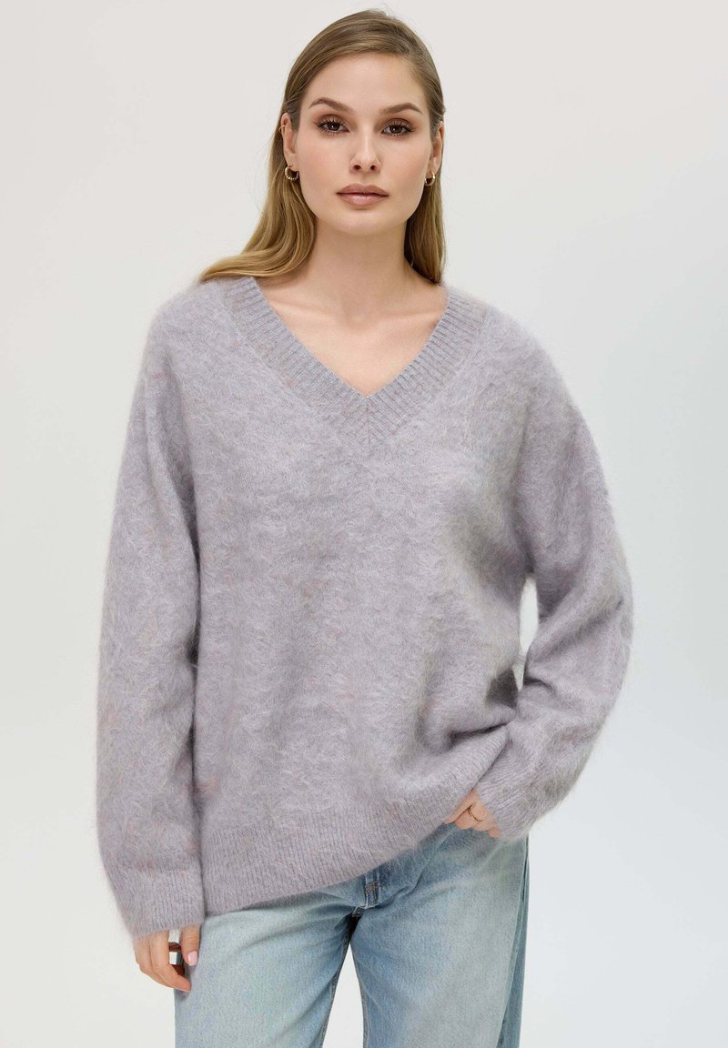 Maglione v-neck di un morbido viola chiaro con spalle scese e polsini a costine. Indossato sopra jeans azzurri chiari, evidenziando una vestibilità rilassata.