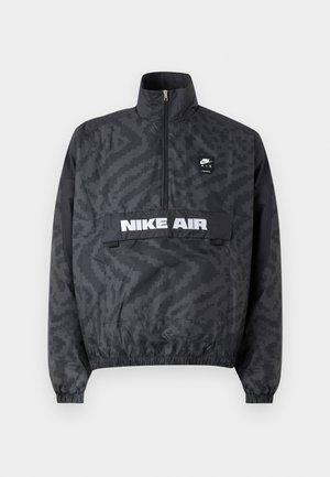 Veste coupe-vent noire Nike Air avec un col haut, une fermeture éclair demi-zippée à l'avant, un motif ton sur ton sur l'ensemble et un logo blanc sur la poche poitrine. Poignets élastiques.
