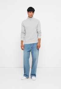 Svijetlo sivi turtleneck pulover s rebrastim manžetama i rubom, uparen s labavim svijetloplavim trapericama i bijelim tenisicama. Jednostavan, ležeran outfit.