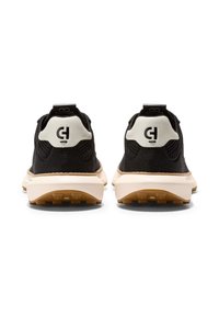 Černé sportovní boty s strukturální svrchní částí, bílými akcenty na patě a světlou mezipodešví. Jsou vybaveny logem na zadní straně a gumovou podešví.