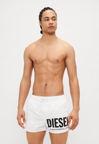 White swim shorts featuring a bold black "DIESEL" logo and text, with a drawstring waist and a smooth, lightweight fabric.