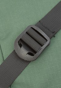 Eine grüne Stoffoberfläche mit einer schwarzen Kunststoffschnalle und einem Riemen, der die Details der Schnalle vor dem strukturierten Hintergrund hervorhebt.