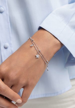 Pulsera de plata con múltiples cadenas que presentan dijes en forma de estrella y acentos esféricos. Se lleva en la muñeca, destacando su diseño delicado.