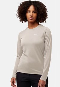 Licht beige shirt met lange mouwen, gemaakt van zachte stof. Heeft een ronde hals en subtiele branding nabij de linkerschouder. Soepele textuur.