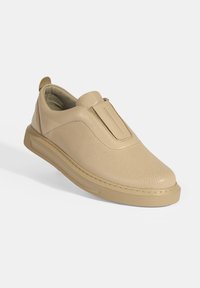 Beige instappers met een geperforeerde leren bovenkant, rubberen zool en een ronde neus. Inclusief een gestikte accent en een achterste trekhaak.