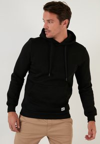 Sudadera con capucha negra, mezcla de algodón, bolsillo canguro, cordones ajustables, puños y dobladillo acanalados, detalle de marca minimalista.