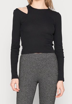 Black long-sleeve top with ribbed texture, featuring an asymmetrical shoulder cut-out design. Paired with textured gray high-waisted pants.