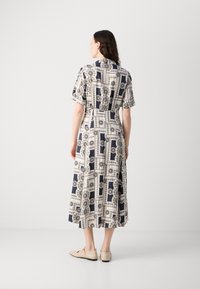Short-sleeve, patterned dress in navy and cream with geometric designs, cinched waist, and mid-calf length. Footwear is beige flats.
