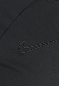 Musta kangas, jossa on ommeltu Nike-swoosh-logo tummemmassa sävyssä. Liukas rakenne, jossa on matta pinta eikä näkyviä kuvioita.
