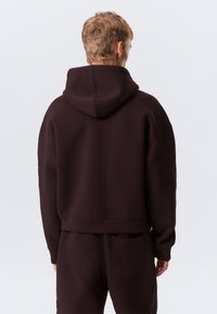 Brun hettegenser laget av mykt materiale med en avslappet passform, med kengurulomme, ribbede mansjetter og et teksturert design på ermene.