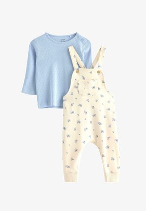 Chemise bleu clair à manches longues avec un motif texturé, assortie à une salopette couleur crème ornée d'un imprimé floral et de boutons latéraux.
