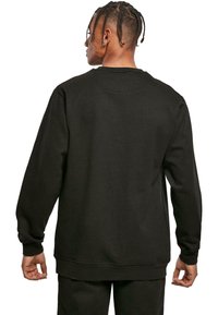 Felpa nera con maniche lunghe, colletto tondo e polsini e orlo a coste. Tessuto morbido con un design semplice e minimale.