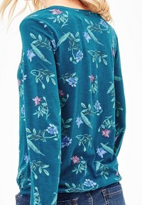 Turkos långärmad topp med blommönster i blått och rosa, mjuk textur, avslappnad passform och rundad halsringning.