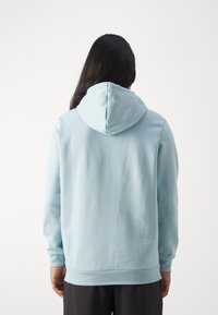 Vaaleansininen huppari, jossa on suuri huppu, pitkät hihat ja resorit hihansuissa. Valmistettu pehmeästä, sileäpintaisesta kankaasta. Minimalistinen muotoilu.