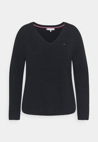 Pull noir en maille avec col en V, manches longues et petit logo rouge, blanc et bleu sur la poitrine gauche.