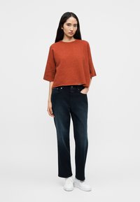 Πουλόβερ σε σκουρόχρωμο ρινίσμα, ευρύχωρο με φαρδιά μανίκια, συνδυασμένο με σκούρο μπλε, άνετο τζιν. Λευκά αθλητικά παπούτσια ολοκληρώνουν την εμφάνιση.