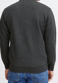 Szary, teksturowany sweatshirt z prążkowanymi mankietami i dolnym ściągaczem, z delikatnym poziomym wzorem pasków, w połączeniu z niebieskimi dżinsami.