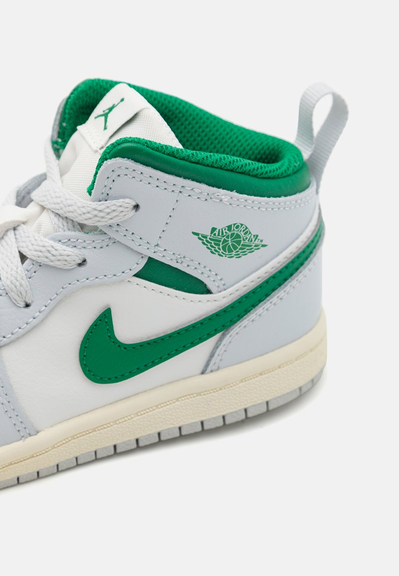 Zapatilla de cuero blanca con acentos verdes, que presenta un acabado suave, cierre de cordones y un logo de Air Jordan visible en el lateral.
