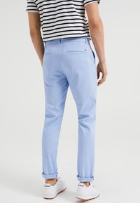 Ljusblå byxor i slim fit, med bakfickor och uppvikta fållar, kombinerat med vita sneakers och en randig skjorta.