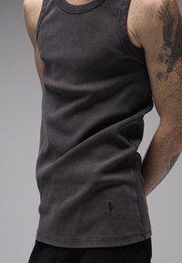 Σκούρο γκρι ριπ αμάνικο τοπ από μαλακό υλικό, με στρογγυλή λαιμόκοψη, καθαρές άκρες και μικρό λογότυπο της μάρκας στο τελείωμα.