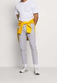 Bílé tričko, žlutá mikina uvázaná v pase, pruhované kalhoty v bílé a námořnické modři a světlé tenisky se šedými detaily.