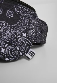 Marsupio nero in tessuto con motivo paisley bianco, superficie testurizzata, chiusura con zip e etichetta del marchio sul lato.