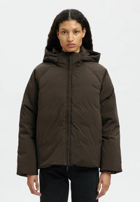Giacca a vento marrone con zip frontale, cappuccio e maniche ampie. Tessuto liscio con finitura opaca. Progettata per calore e comfort.
