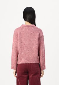 Maglione lavorato a maglia di un morbido rosa con macchie texture, design corto, maniche ampie e orlo a coste. Abbinato a pantaloni in velluto a coste borgogna.