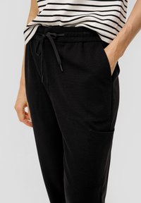 Zwarte sweatpants van zacht materiaal, met een elastische tailleband met trekkoord, zijzakken en een extra patch pocket.
