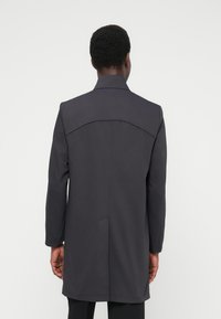 Ciemnoszary płaszcz z usztywnionym kołnierzem, długimi rękawami, prostym krojem i minimalnymi detalami szwów. Posiada yoke na plecach oraz wsuwane kieszenie.