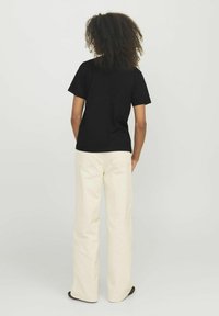 T-shirt nera a maniche corte abbinata a pantaloni a gamba larga color crema. Il T-shirt ha un design semplice; i pantaloni presentano tasche posteriori e una texture liscia.