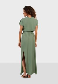 Robe maxi en tissu vert avec une coupe décontractée, dotée de manches courtes, d'une taille cintrée et d'une fente sur le côté pour faciliter les mouvements.