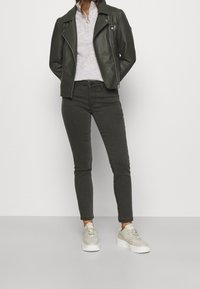 Zwarte leren motorjack, lichtgrijs sweater, donkergrijze skinny jeans en beige sneakers met een witte zool. Geen opvallende patronen of hardware.