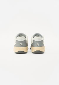 Beige and grey sneakers with a textured finish, featuring a soft upper, padded collar, and rubber outsole. Logo detail on heel.