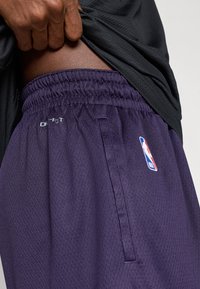 Μώβ αθληματικά σορτς με πλέγμα και ελαστική μέση, που διαθέτουν πλαϊνή τσέπη και το λογότυπο του NBA; αναπνεύσιμο ύφασμα με υφή.