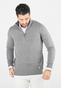 Pull à zip gris avec col, poignets et ourlet côtelés. Fabriqué en tissu doux, avec un petit logo en bas à gauche.
