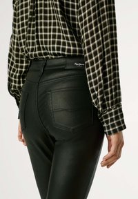 Pantalones de cuero sintético negros con cintura alta, con un diseño de bolsillo trasero y costuras de acento. Combinados con una camisa a cuadros en blanco y negro.