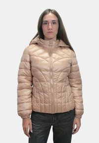 Giacca imbottita in morbido tessuto color sabbia con zip frontale, cappuccio e motivo trapuntato. Presenta polsini arricciati e una silhouette aderente.