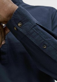 Navy napakauppinirp shirt with a textured fabric; features a cuff with two round buttons and a small slit, showcasing a tailored design.