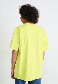 Camiseta de manga corta y corte holgado en algodón amarillo neón. Presenta un cuello redondo, hombros caídos y una textura suave y lisa.
