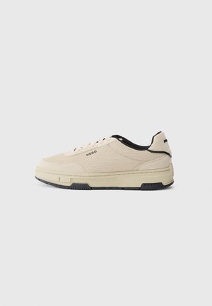 Beige sneaker with a textured fabric upper, black accents on the collar, a thick white sole, and subtle brand logo on the side.
