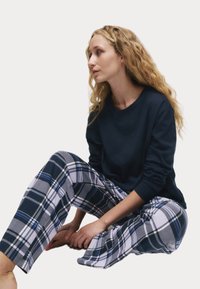 Marineblauwe langermige shirt gecombineerd met grijs geruite broek met blauwe en witte accenten; zachte stof met een ontspannen pasvorm en een recht gesneden ontwerp.