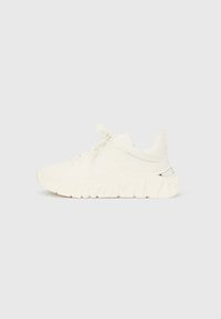 Λευκό αθλητικό παπούτσι με υφή στο πάνω μέρος, επενδεδυμένο κολάρο και ανάγλυφο λογότυπο σε χοντρή σόλα. Διαθέτει αντανακλαστικό στοιχείο στη φτέρνα.