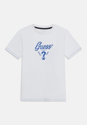 Hvid t-shirt med korte ærmer og blå syninger, med "Guess U.S.A."-logo, der viser et stort blåt spørgsmålstegn og teksten "Washed Jeans" på forsiden.