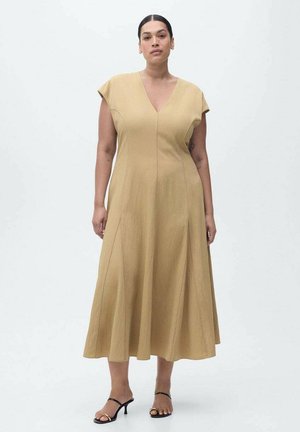 Abito beige a ginocchio con maniche a cappuccio e scollatura a V. Presenta una silhouette a linea A e sottili cuciture verticali. Indossato con sandali neri con tacco.