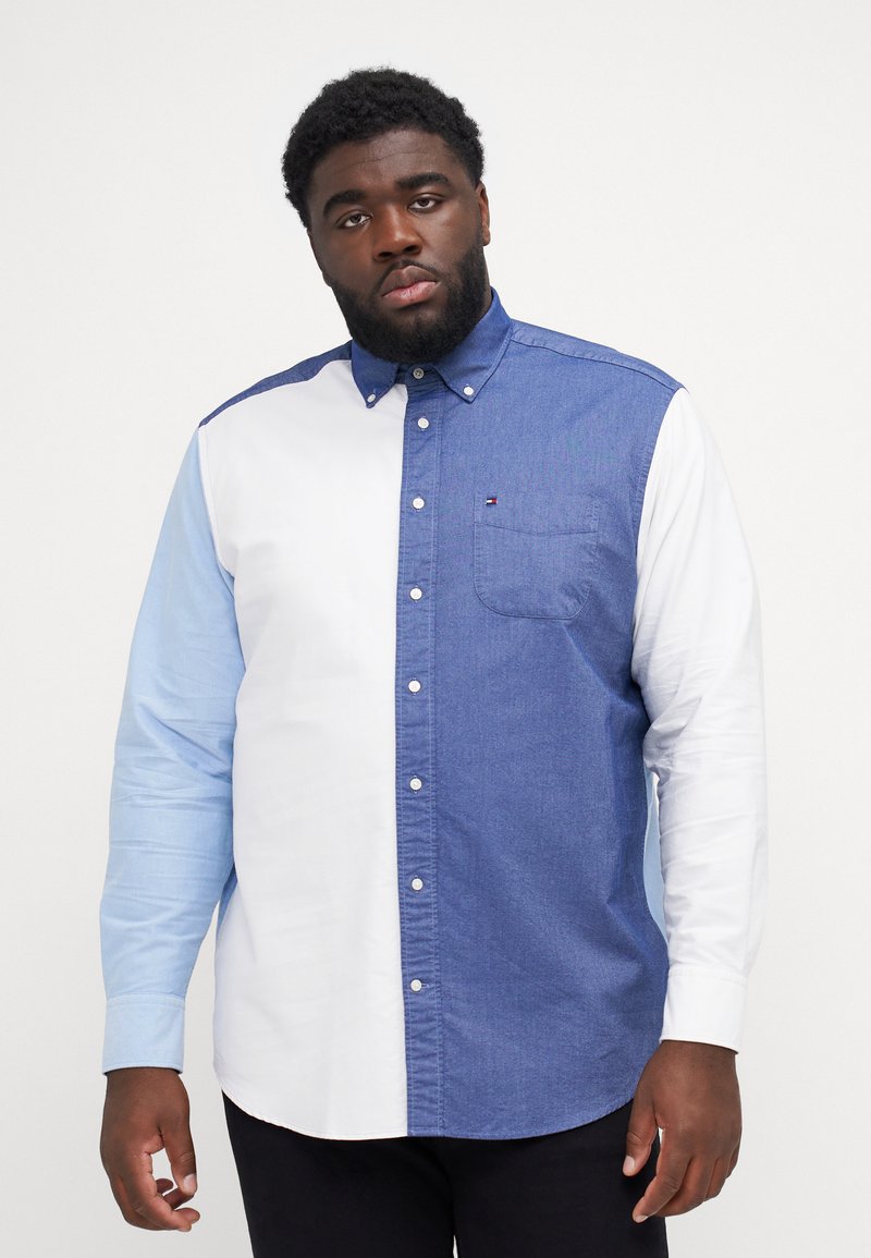 Camicia con bottoni caratterizzata da un design a blocchi di colore, con il lato sinistro in denim scuro, il lato destro in azzurro chiaro e una manica bianca. Taschetta sul petto.
