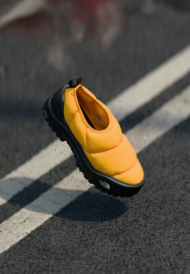 Chaussure jaune rembourrée à enfiler avec une semelle en caoutchouc noire, présentant une surface texturée et une languette arrière pour un enfilage plus facile.