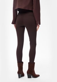 Bruine legging gemaakt van rekbare stof, met een strakke pasvorm. Draagt met bruine suède enkellaarzen en een cropped gestreepte blazer.