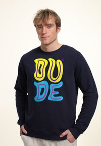 Sudadera azul marino con texto amarillo y azul en negrita que dice "DUDE" en un diseño divertido. Cuello redondo, tejido suave y corte relajado.